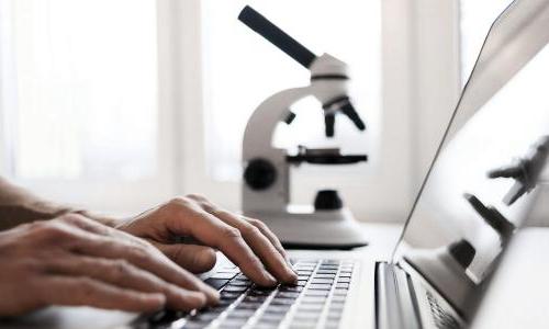 Person typing on laptop with microscope in background